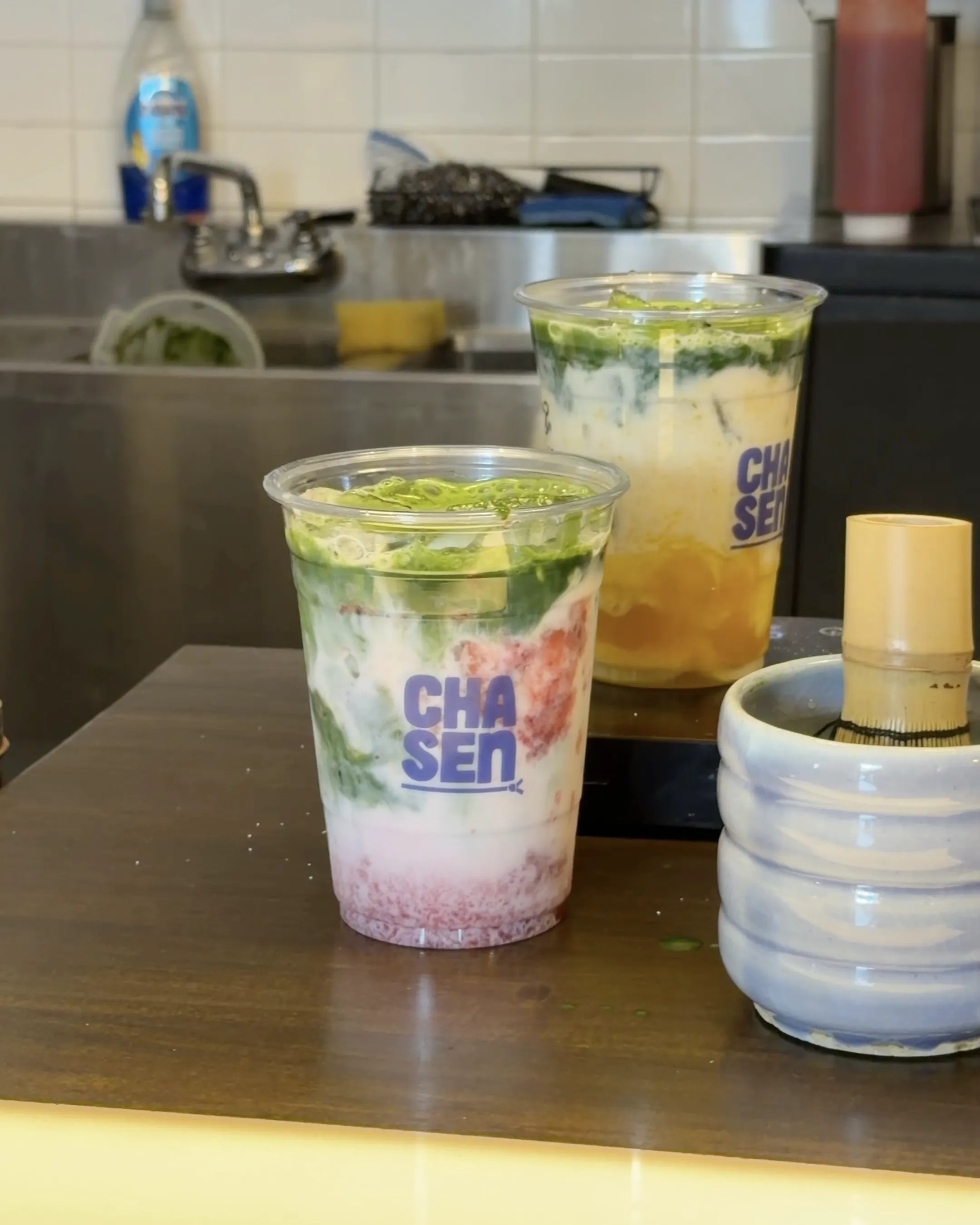 Layered matcha drinks in Chasen cups beside a bamboo whisk
