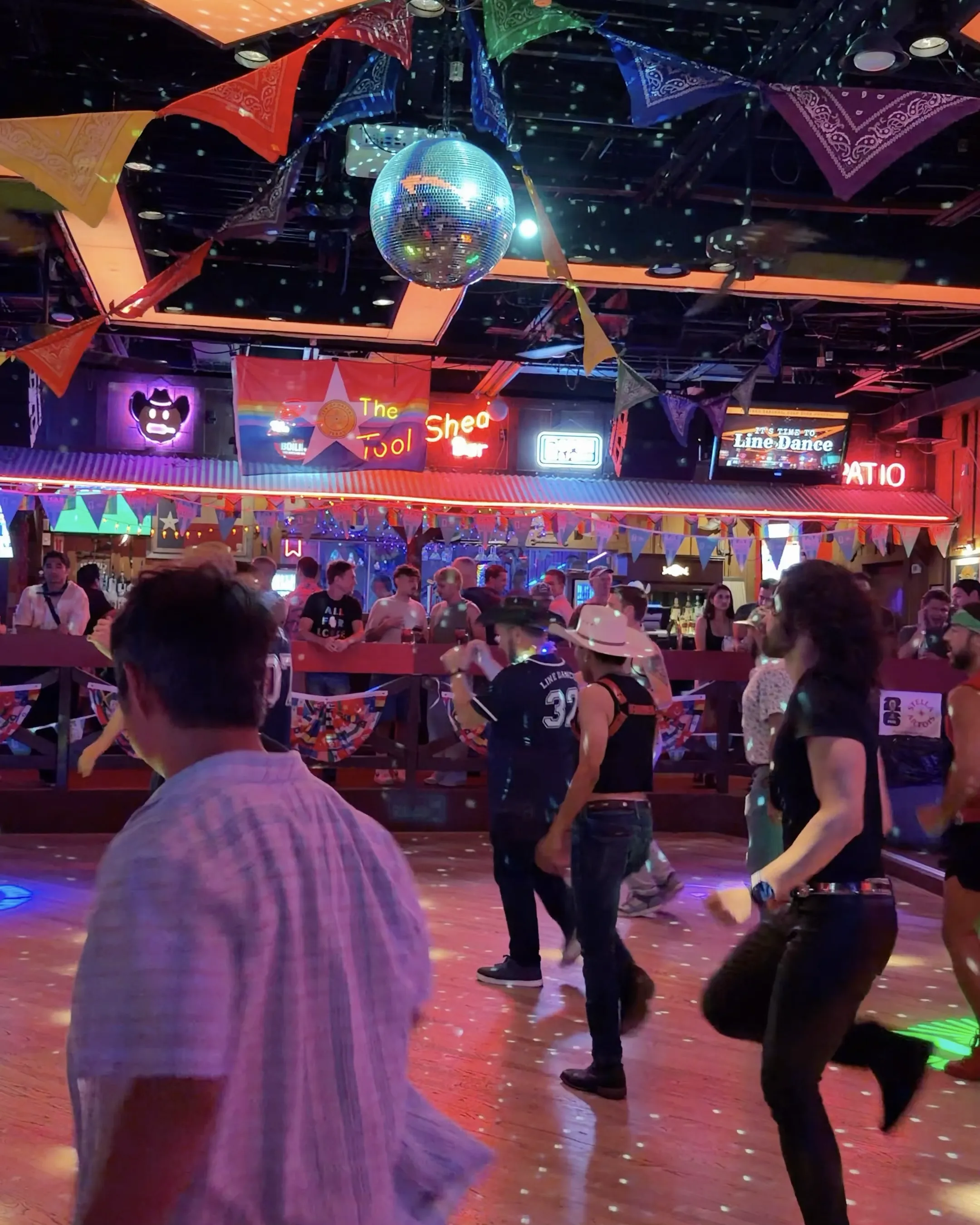 A packed line dancing floor under a disco ball and bunting