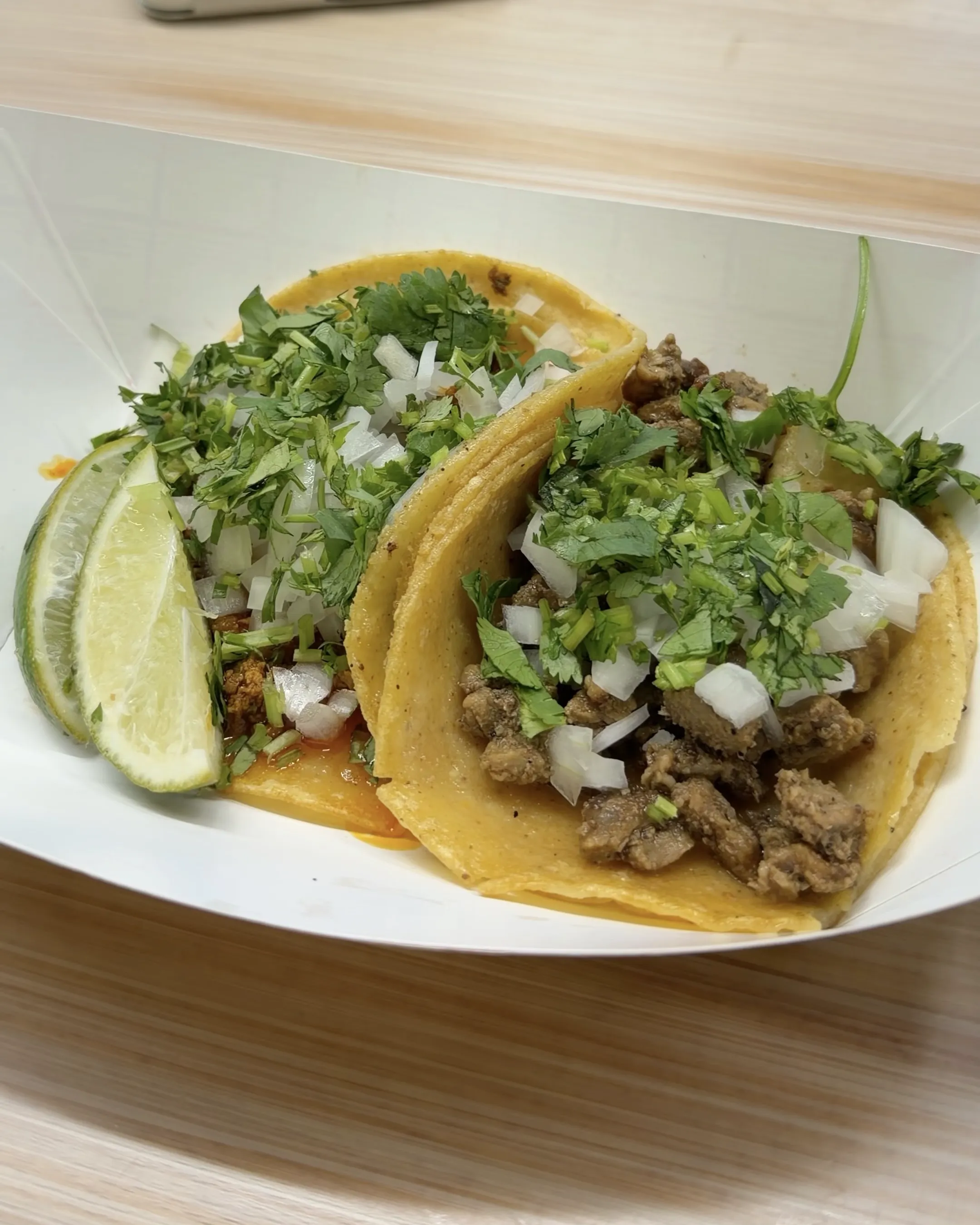 Two tacos loaded with cilantro and onion, with a lime wedge