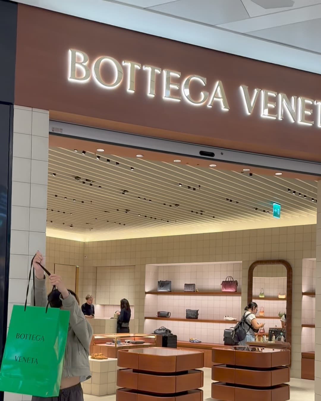 The Bottega Veneta boutique at the Milan airport with a green shopping bag in the foreground