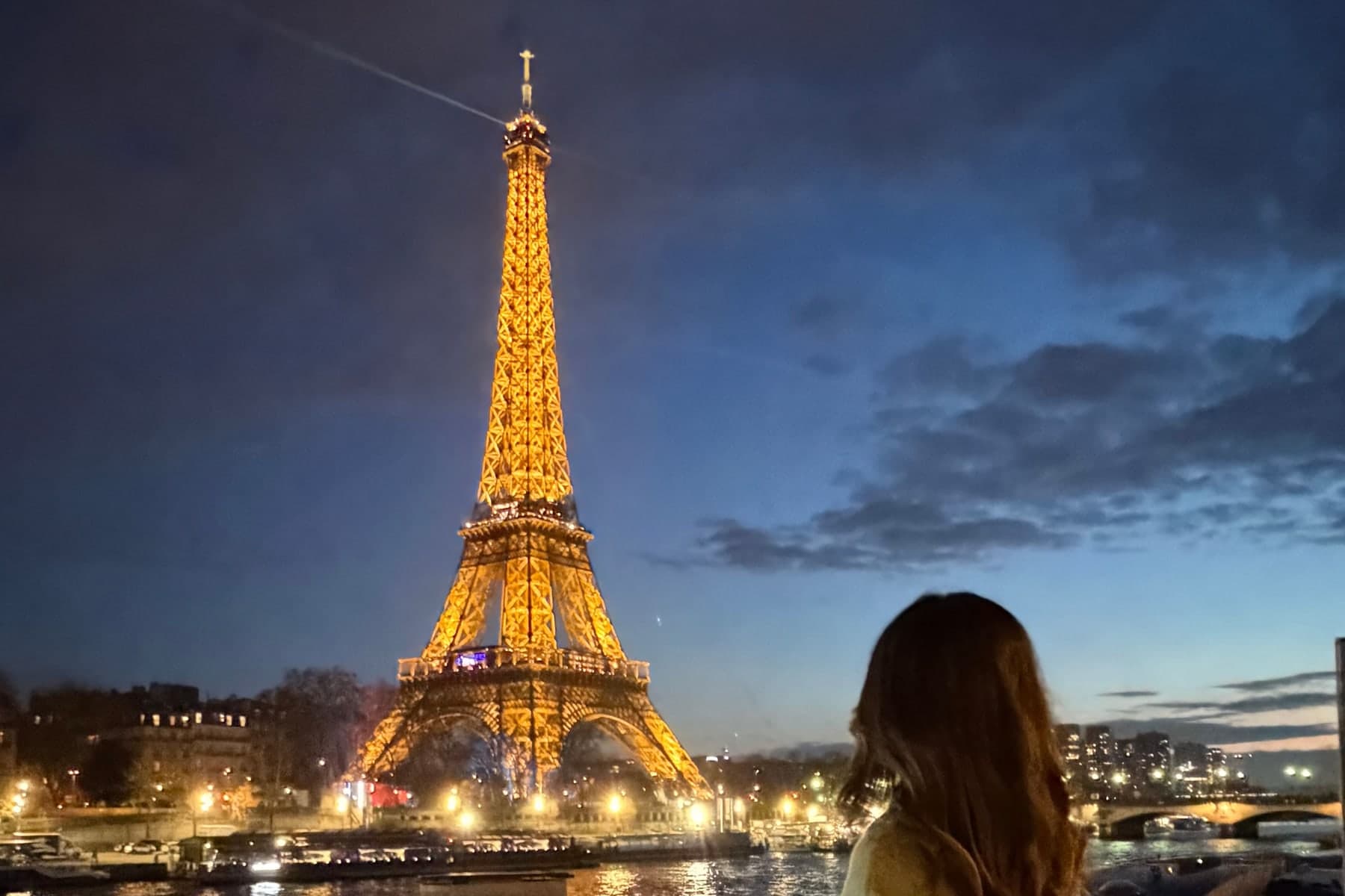 Eileen looking at the Eiffel Tower lit up at dusk from the Seine