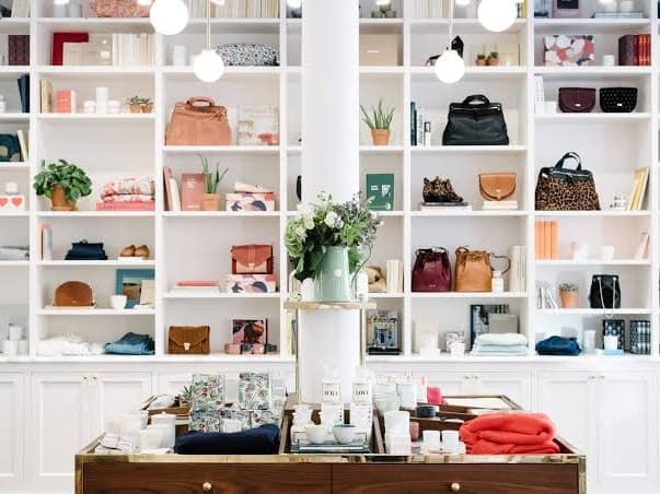 Inside a Sézane store, white shelves of handbags and homeware above a brass-trimmed display table