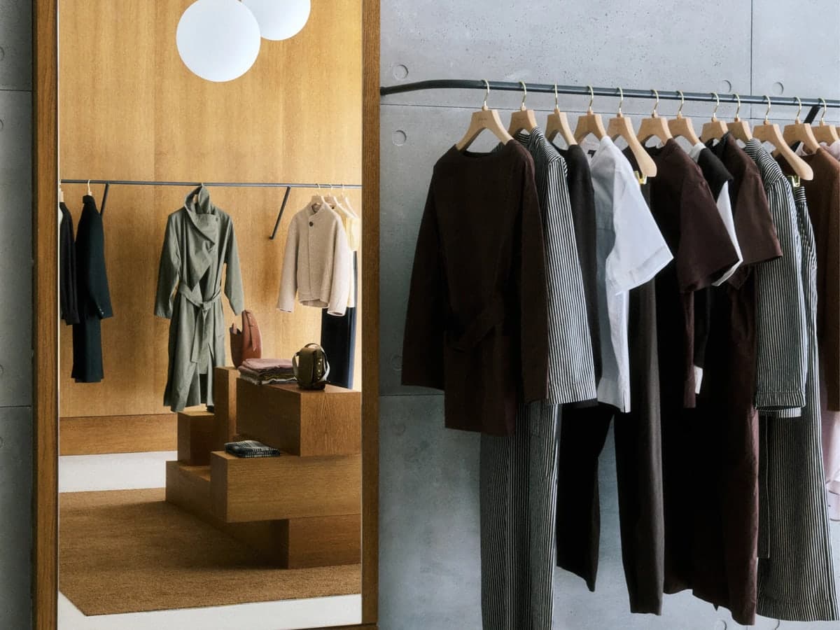 A Soeur store with neutral coats and tops on a rail next to a tall wooden mirror