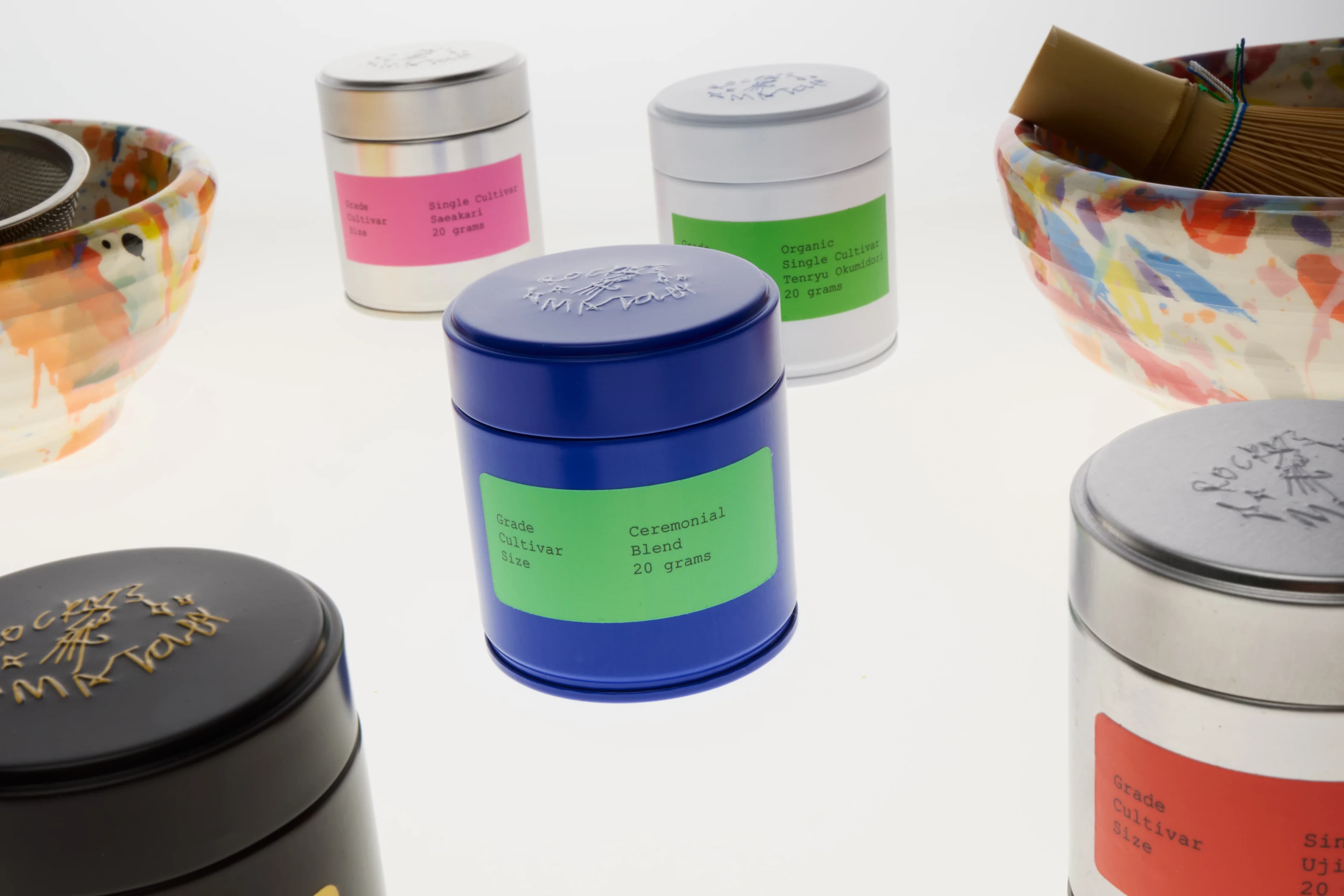 The cobalt blue Rocky's Matcha tin standing out among silver, white and black tins and hand-painted tea bowls