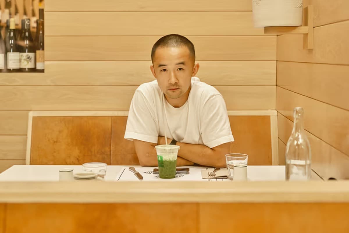 Rocky Xu sitting at a wooden café table with an iced matcha in front of him