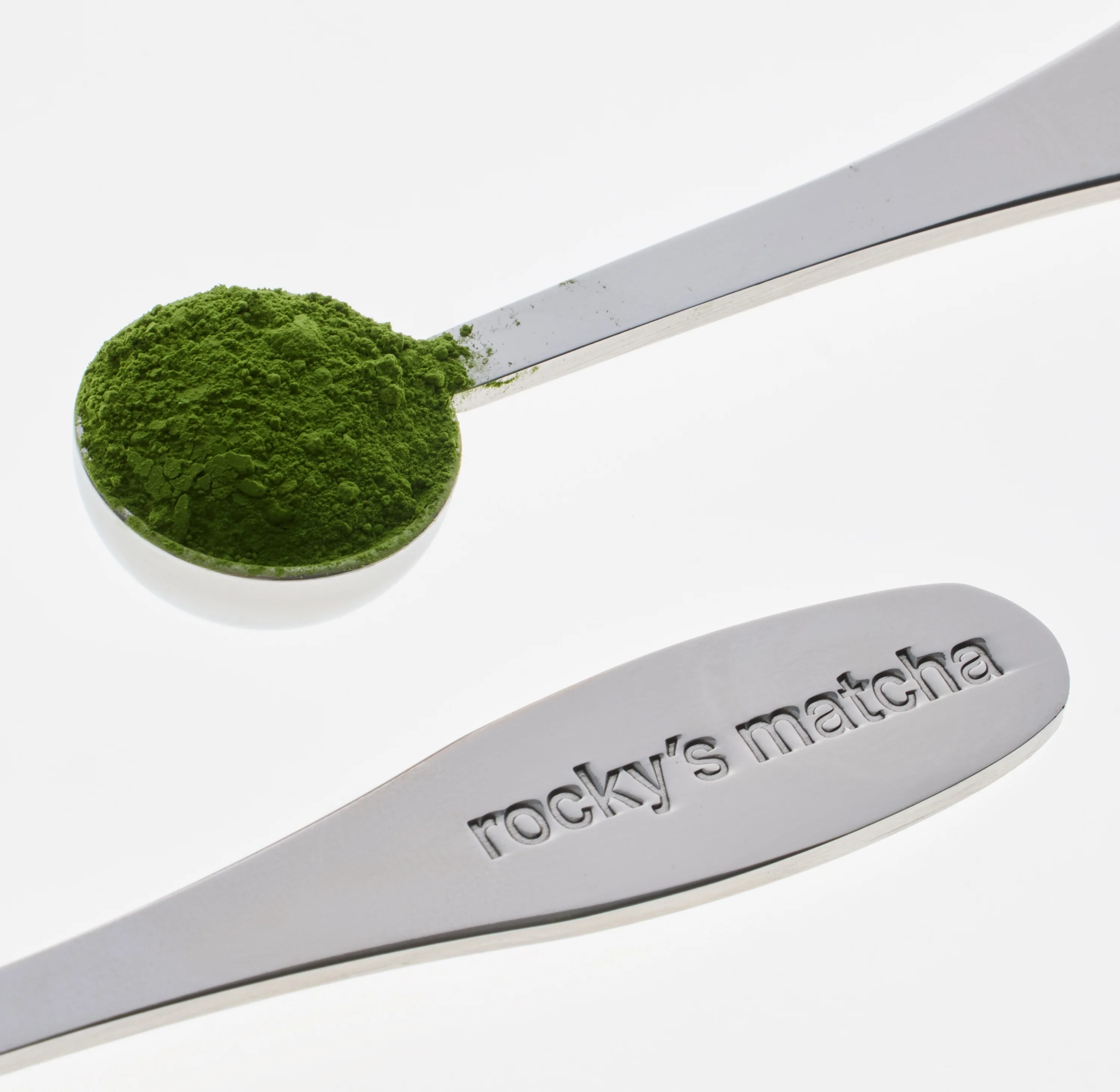 A branded Rocky's Matcha measuring spoon holding a scoop of vivid green matcha powder